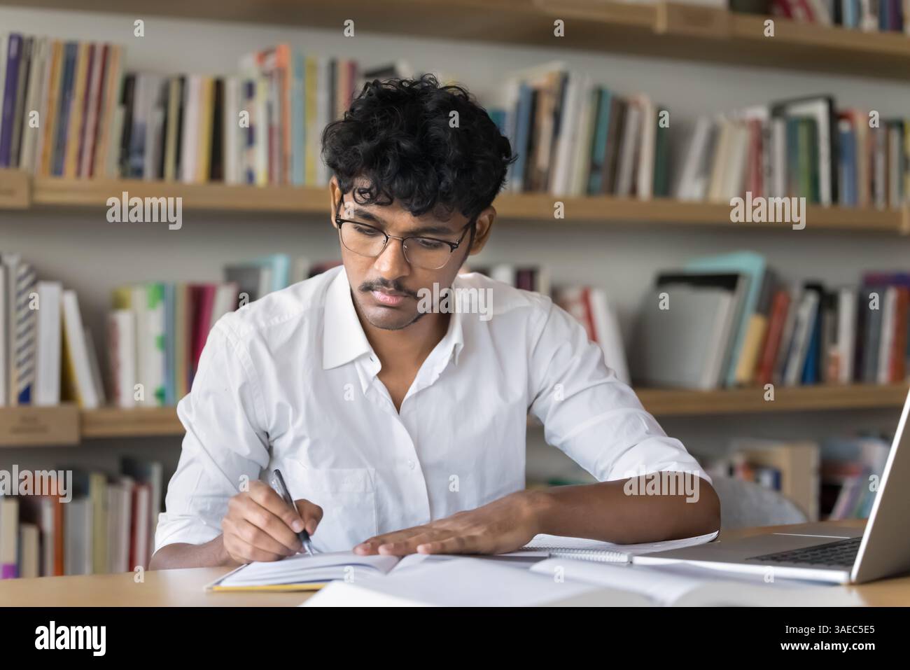 Young male student in glasses studying taking notes in library Stock Photo