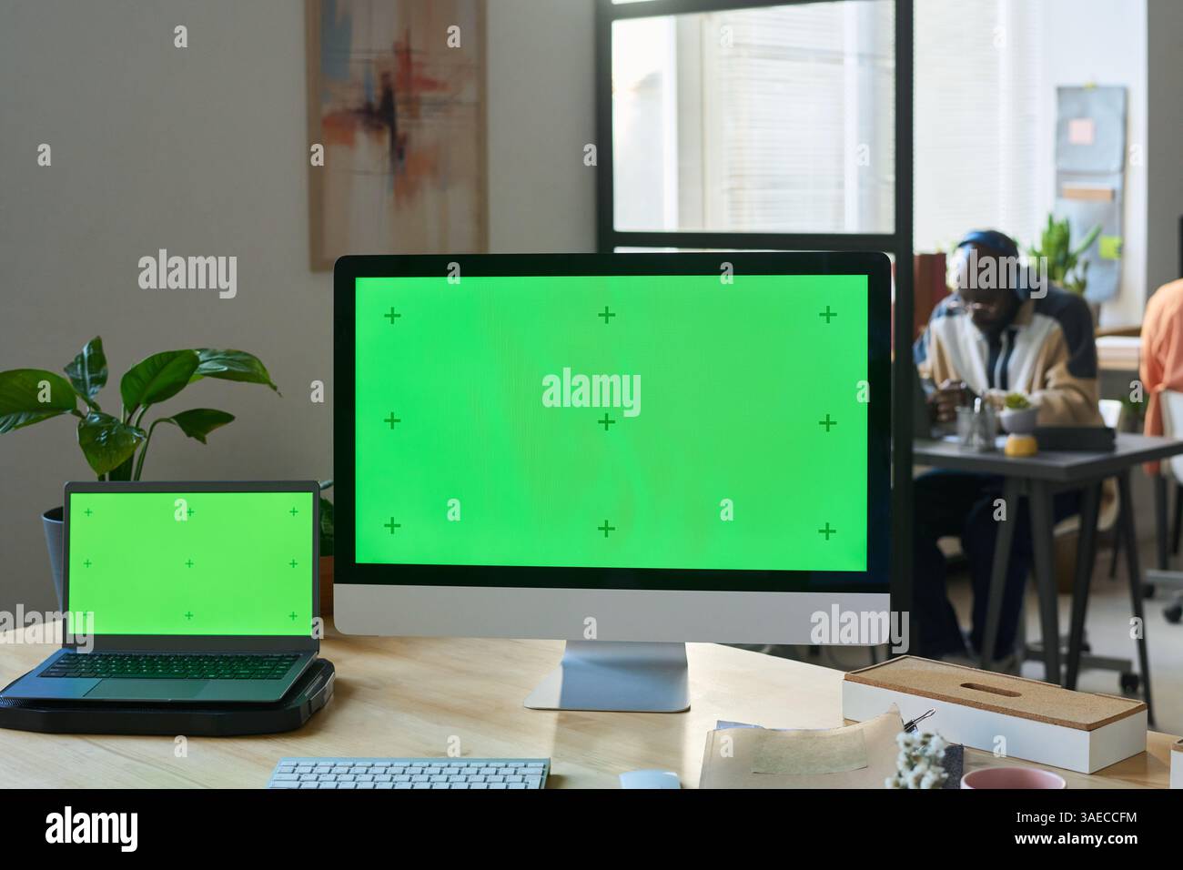 Two blank chromakey screens of laptop and desktop computer standing on desk in front of camera in coworking space Stock Photo