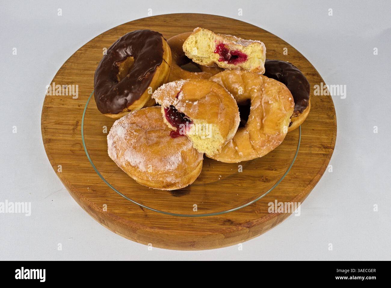 A delicious assortment of donuts, including chocolate glazed and jelly-filled, presented on a rustic wooden tray for a delightful treat on a white Stock Photo