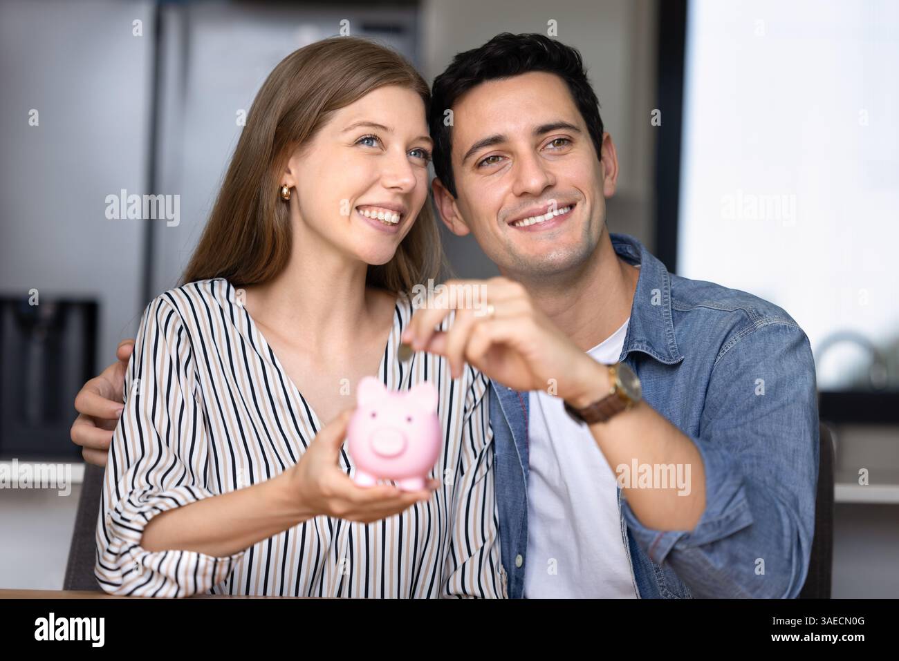 Beautiful young couple placing coin into pink piggy bank Stock Photo ...