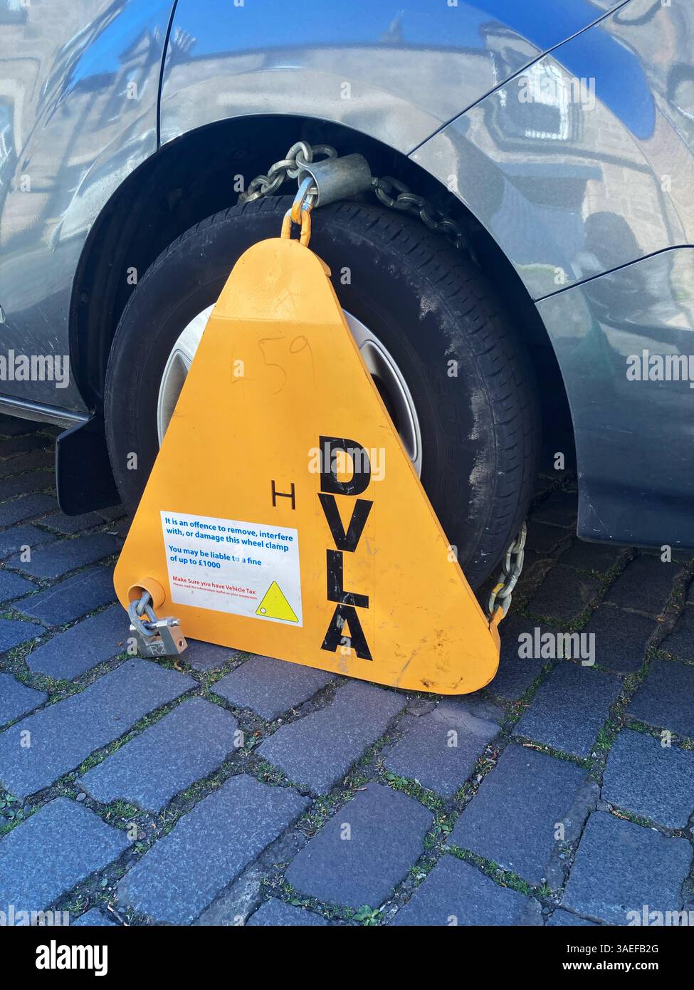 DVLA wheel clamp immobilising a car, in most cases used on cars with unpaid tax or unpaid insurance - Smartphone Captured Stock Image