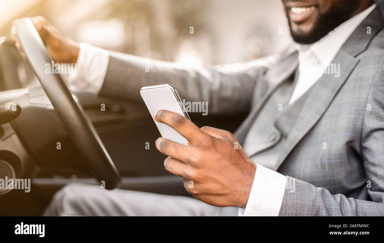 Black guy in suit using smartphone while driving Stock Photo