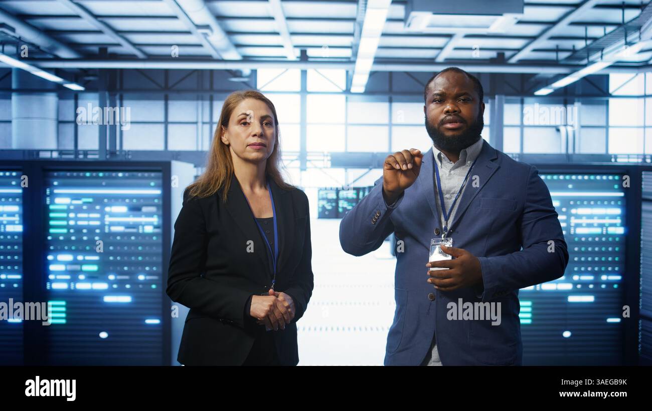 Teamworking technicians in high tech data center workspace looking at hologram visualization. Programmer and colleague working on securing server room hardware using AR tech, camera B Stock Photo