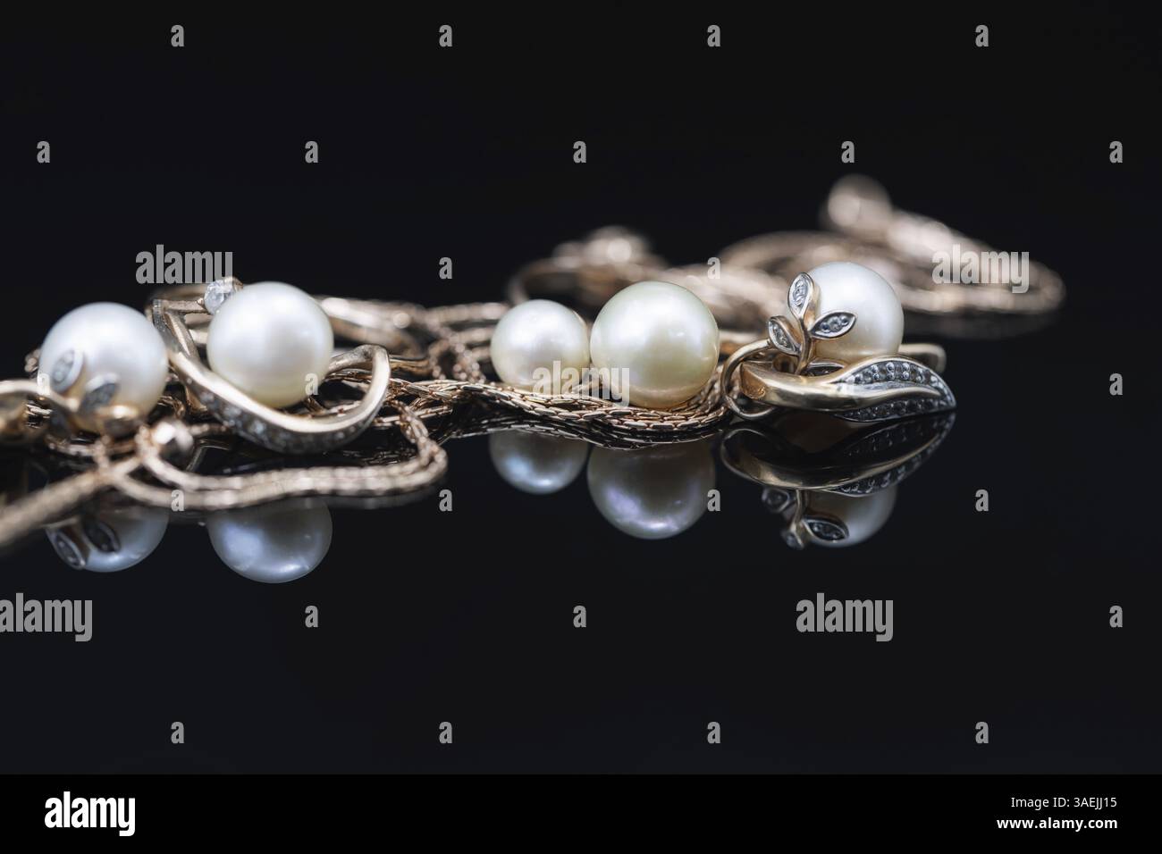 Gold earrings and rings with white pearls lie on a black mirror surface Stock Photo