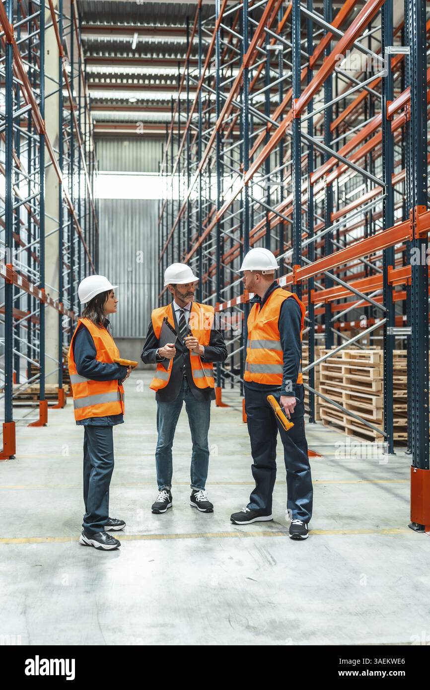 Warehouse workers and their manager are having a discussion about logistics operations inside a large distribution center Stock Photo
