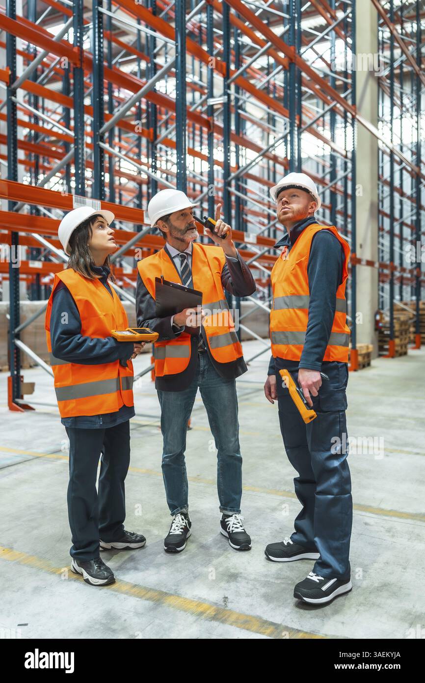 Warehouse workers and their manager are discussing logistics while using a walkie talkie and barcode reader Stock Photo
