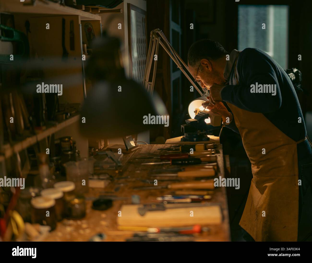 Luthier is meticulously carving a piece of wood. Secured in a vise on ...