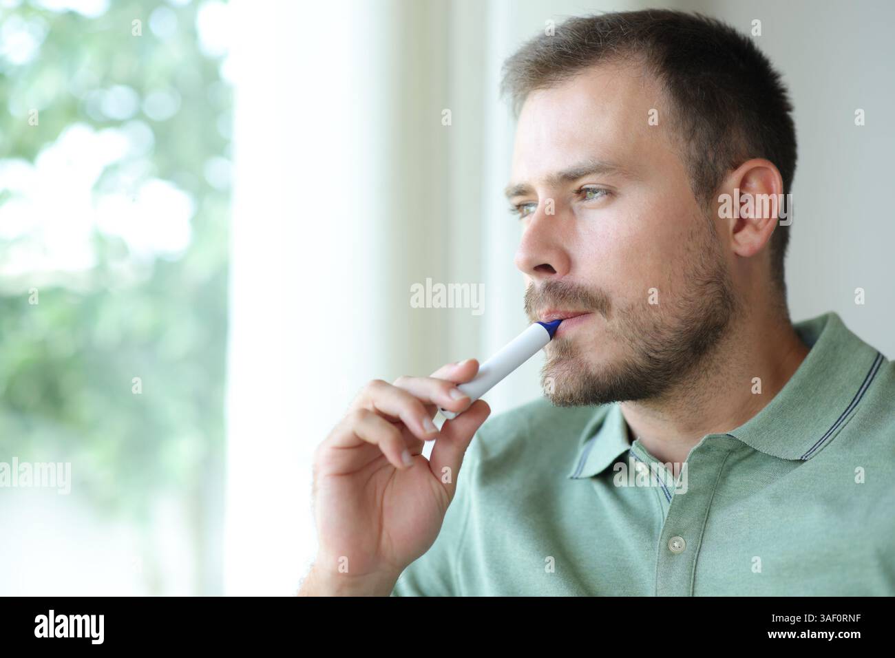Handsome man vaping looking through a window at home Stock Photo