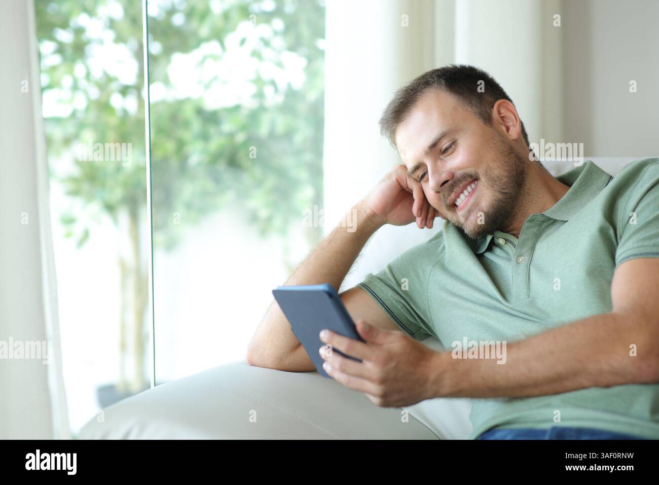 Happy man enjoying reading an ebook sitting on a sofa in a house interior Stock Photo