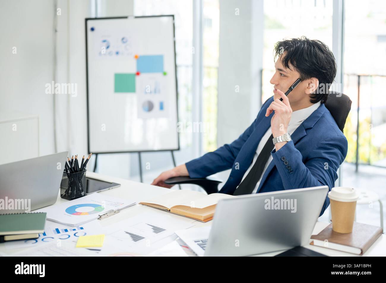 Businessman or male office worker is thinking thoughtfully while holding at pen to his temples. thinking thoughtfully while sitting in the office. Stock Photo