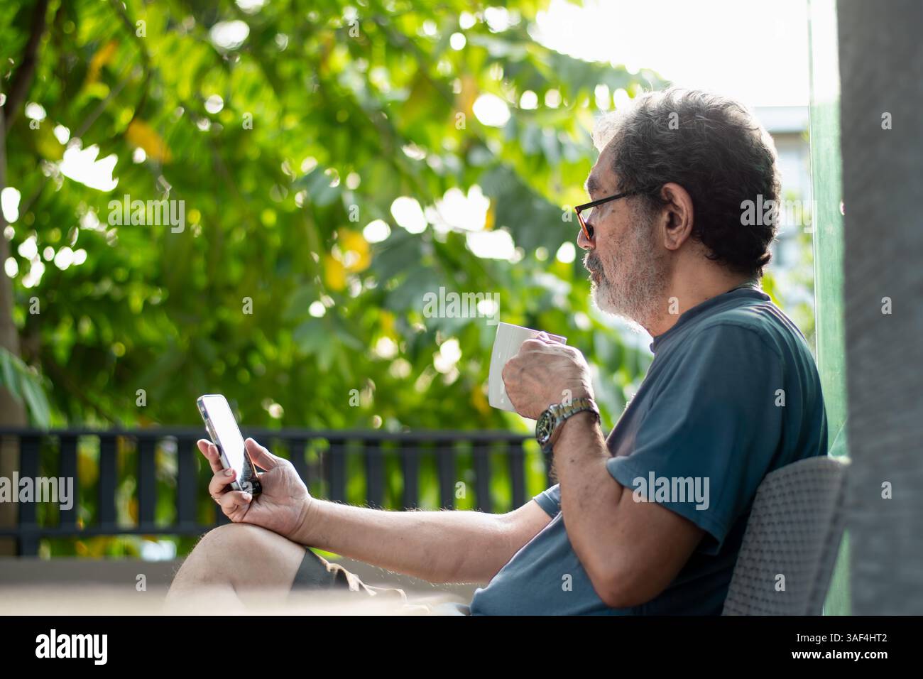 Senior Man using phone outdoors while drinking coffee at home Stock Photo