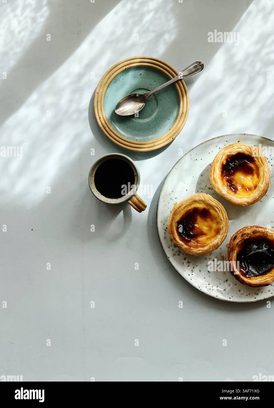 Three Portuguese pastel de nata and cup of black coffee on elegant and modern ceramics. Clean look, light background and shadows, top view Stock Photo