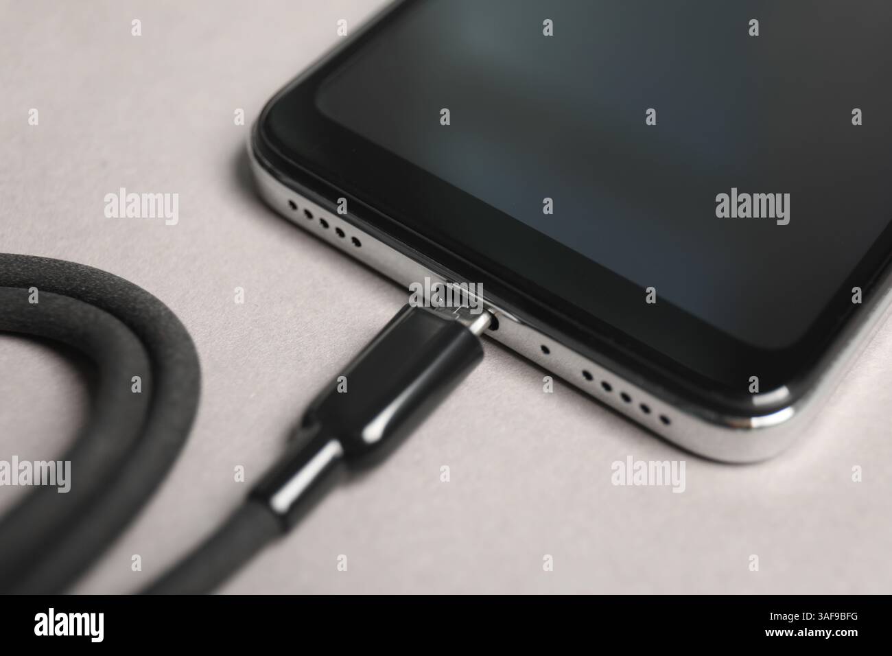 USB charge cable connected to smartphone on light grey background, closeup Stock Photo