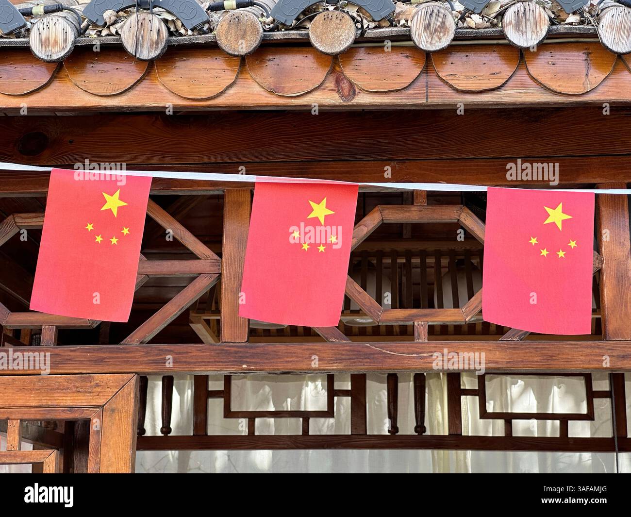 Chinese flags with a star design hanging on a traditional wooden structure, cultural. - Smartphone Captured Stock Image