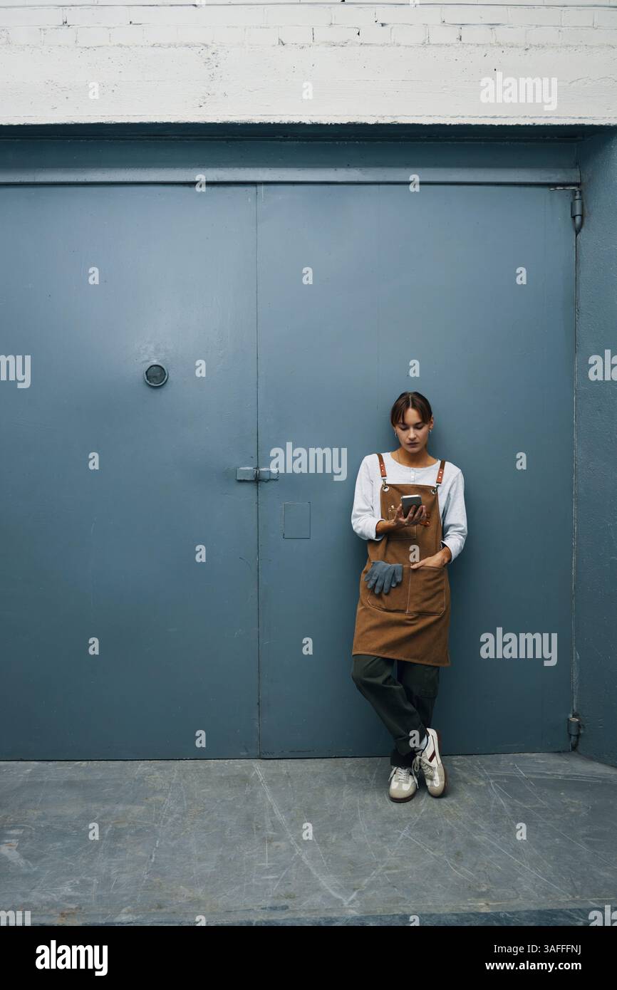 Female Worker Using Phone In Workshop Stock Photo