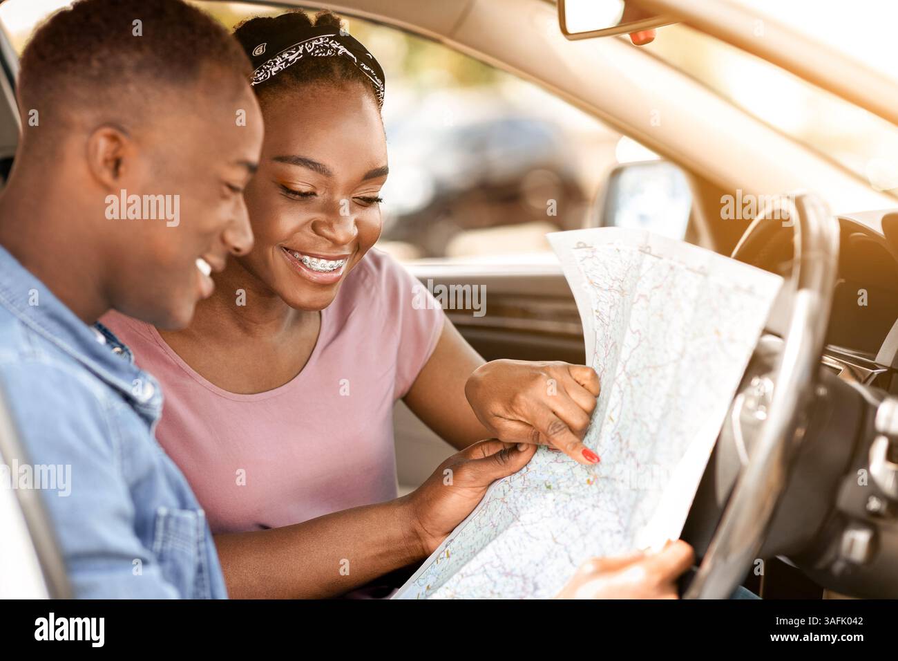 Enthusiastic black couple reading map while having car trip Stock Photo