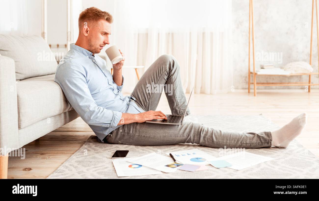 Focused man sitting on floor using phone drinking coffee Stock Photo