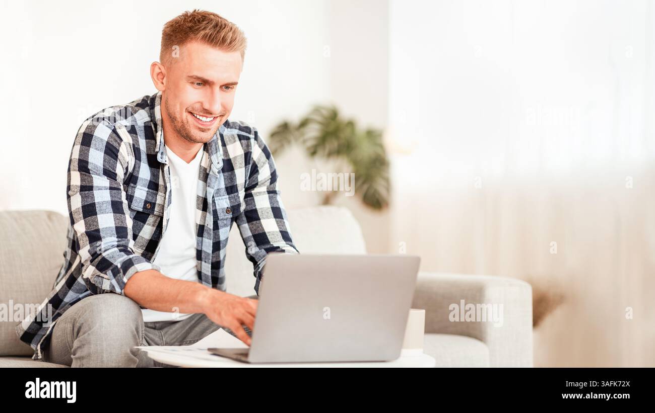 Happy man using laptop sitting on couch Stock Photo