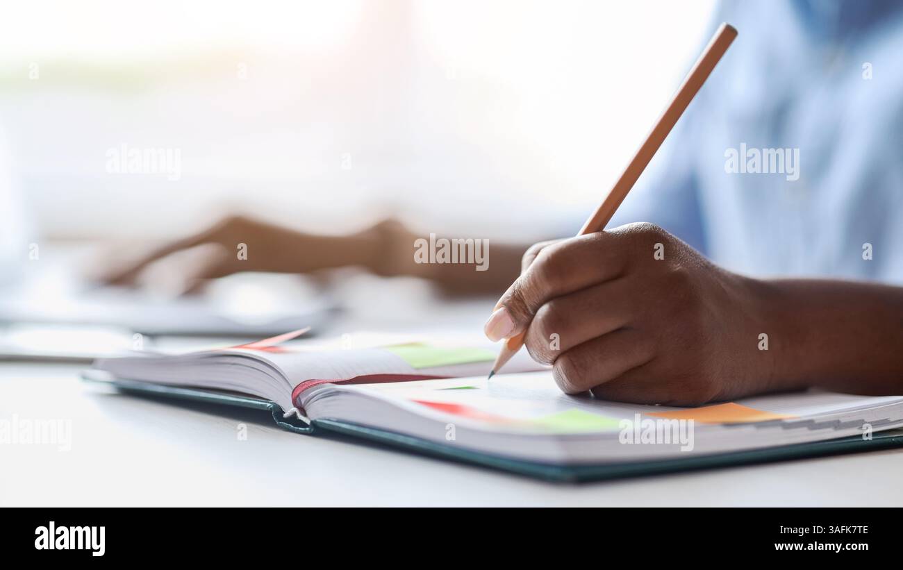 Unrecognizable african female secretary taking notes while working on laptop in office Stock Photo