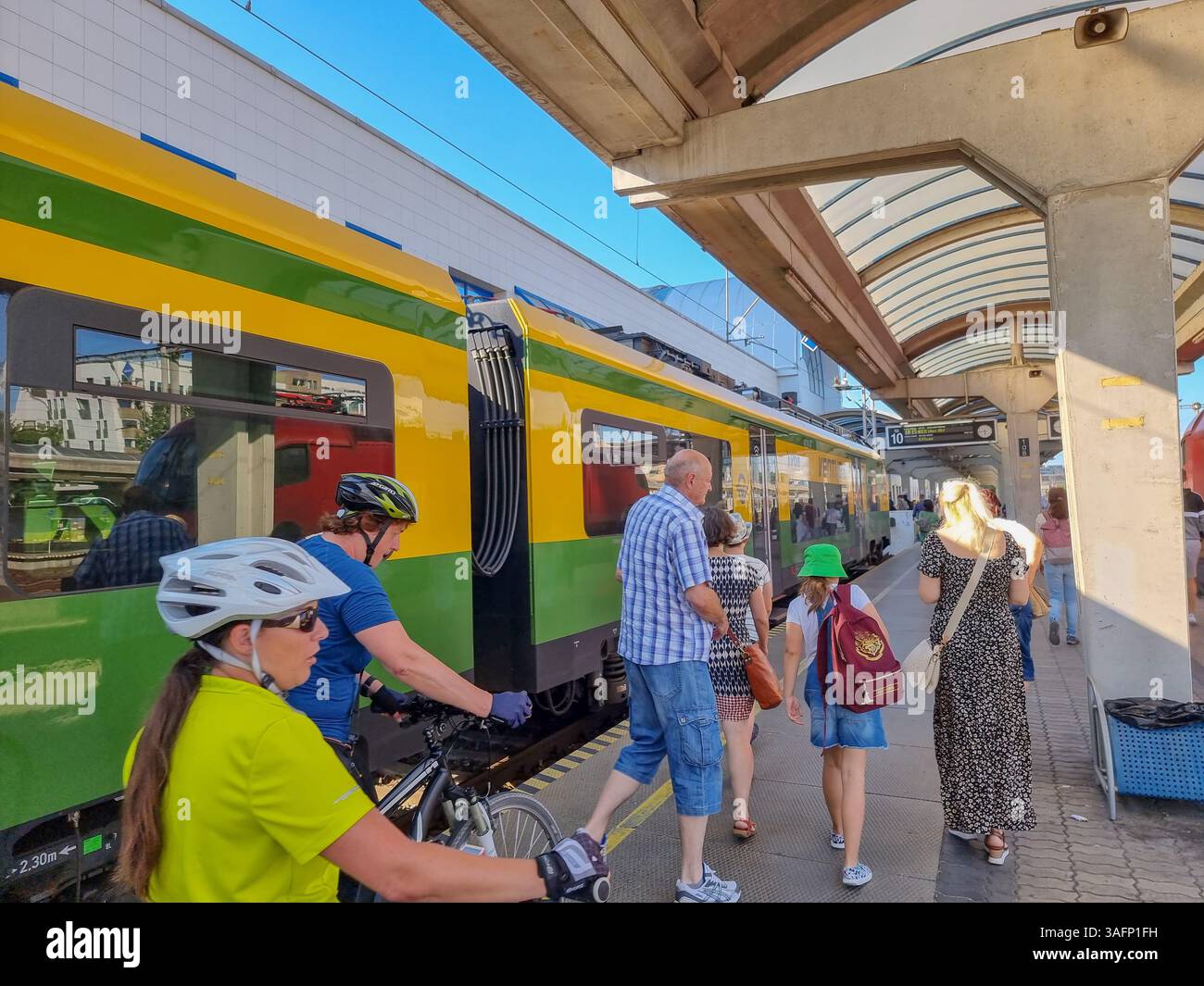 Passengers leaving yellow/green train (from Vienna), some with bicycle, on platform of Bratislava Petrzalka station, Slovakia on a sunny day - Smartphone Captured Stock Image