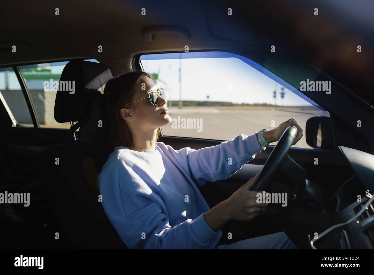 Woman driving and basking in sunlight, wearing sunglasses Stock Photo