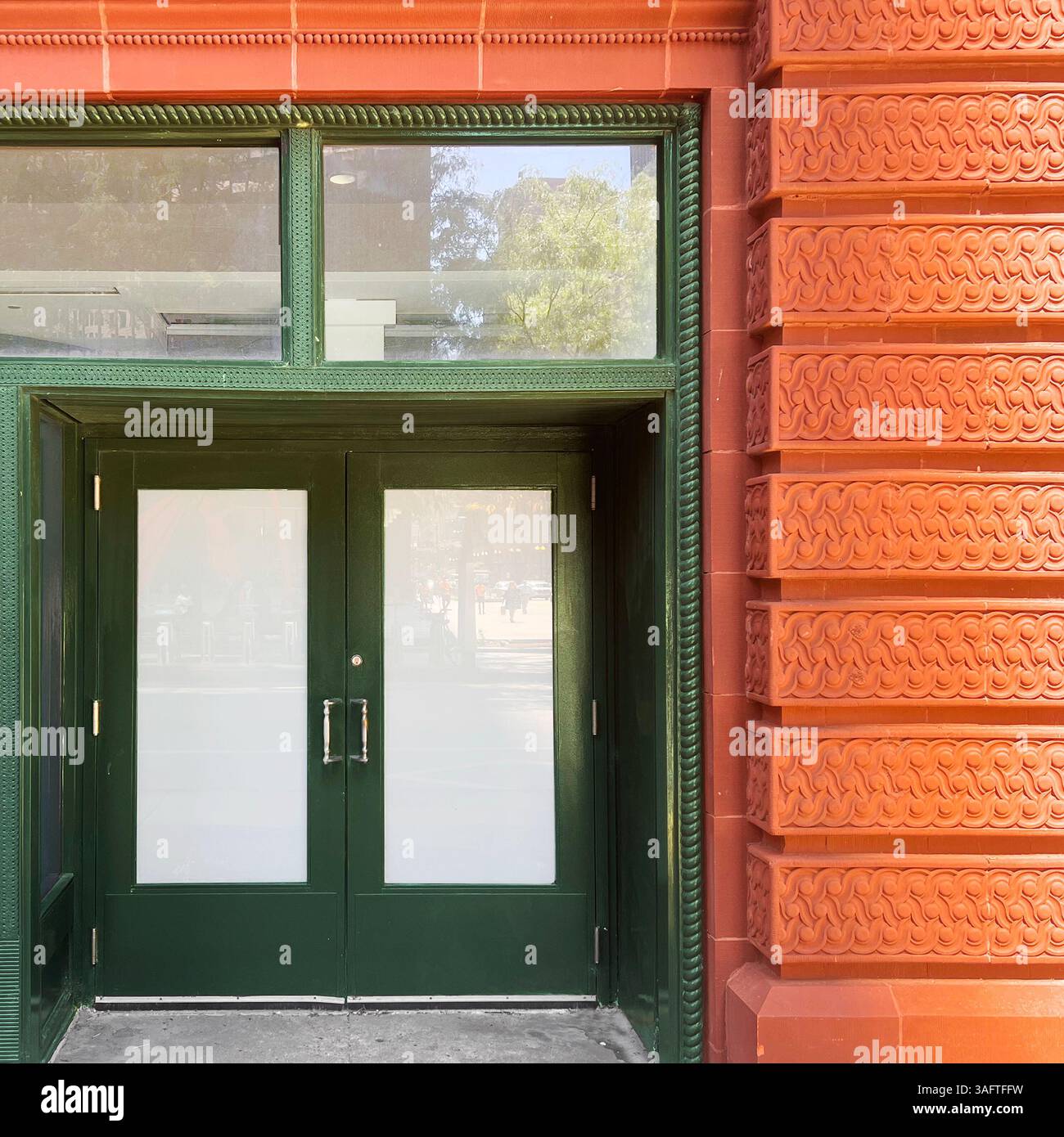 Glossy green double doors with frosted glass set into a richly textured terracotta facade in downtown Chicago - Smartphone Captured Stock Image