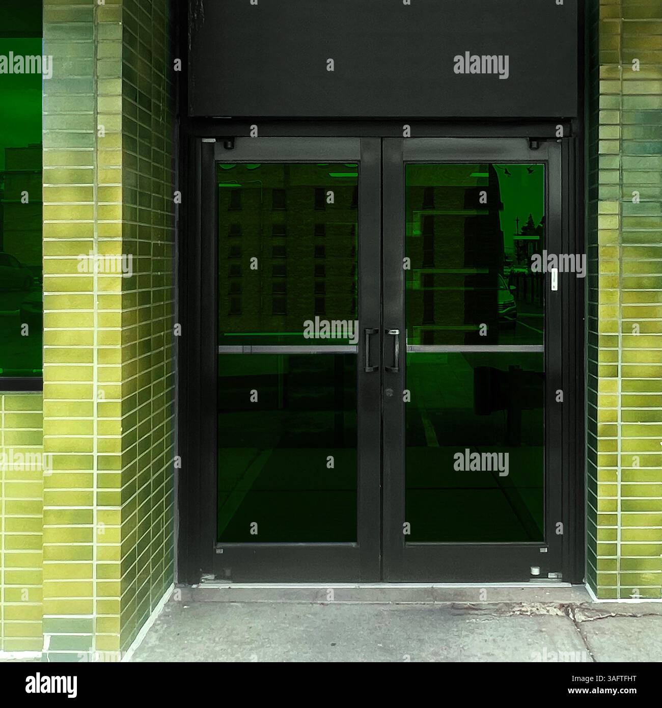 Glossy green tiles wrap around a modern storefront facade in Chicago, framing dark glass doors with a sleek, industrial edge - Smartphone Captured Stock Image