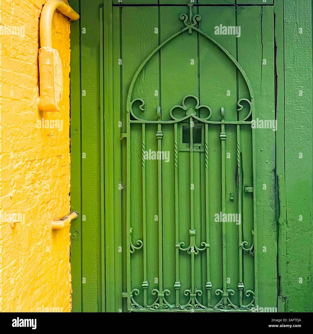 Bright green wrought iron gate with ornate detailing set against a vivid yellow brick wall in a vibrant Chicago alleyway - Smartphone Captured Stock Image