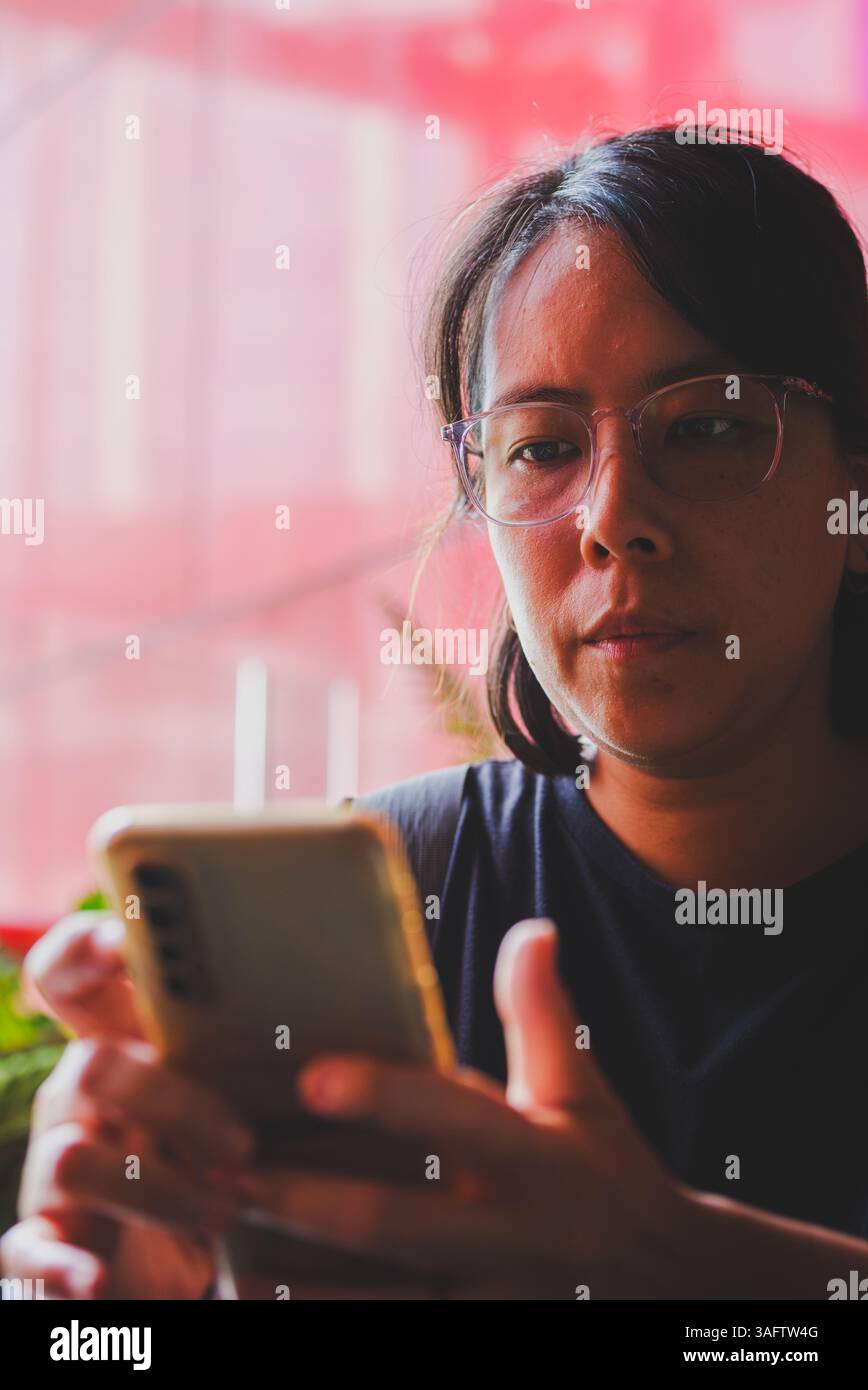 The woman is sitting while looking at her smartphone. Stock Photo
