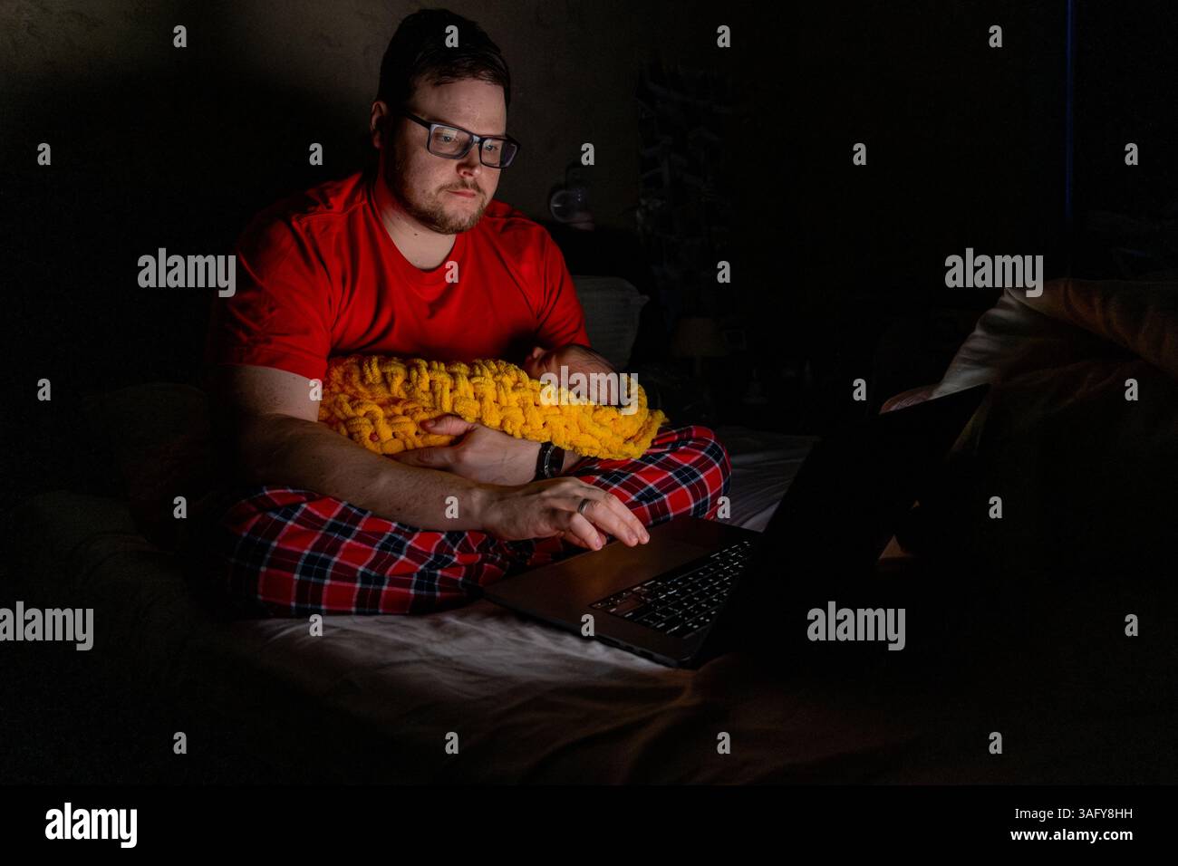Father Holding Baby While Using Laptop in Dim Light Stock Photo