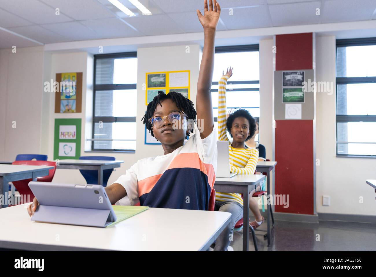 In school, diverse students raising hands while using tablet in classroom Stock Photo