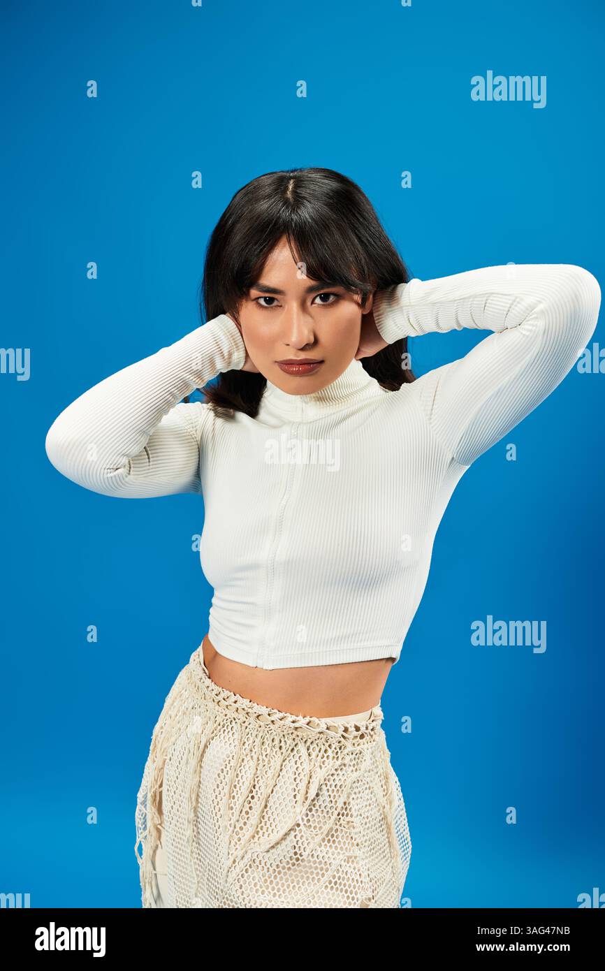 A young Asian woman poses confidently with hands on her head against a ...