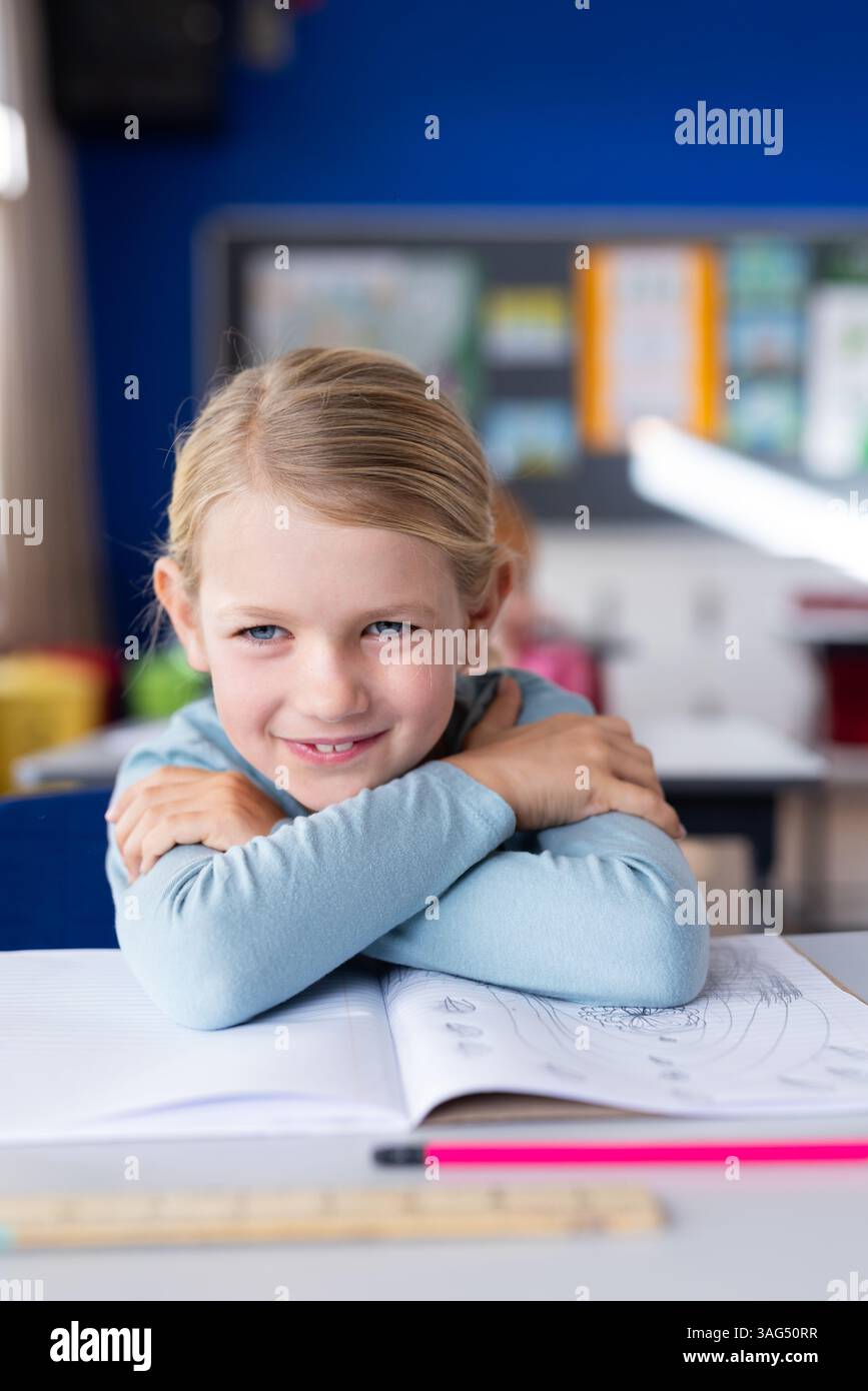 Smiling girl in school classroom sitting at desk with open notebook ...