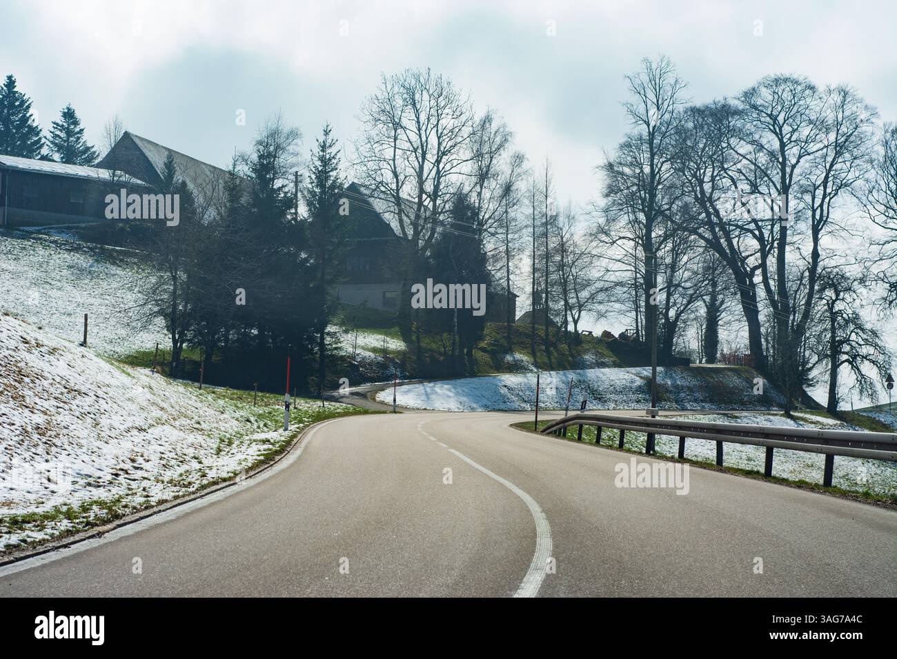 A serene winter day reveals a winding road bordered by white snow and ...