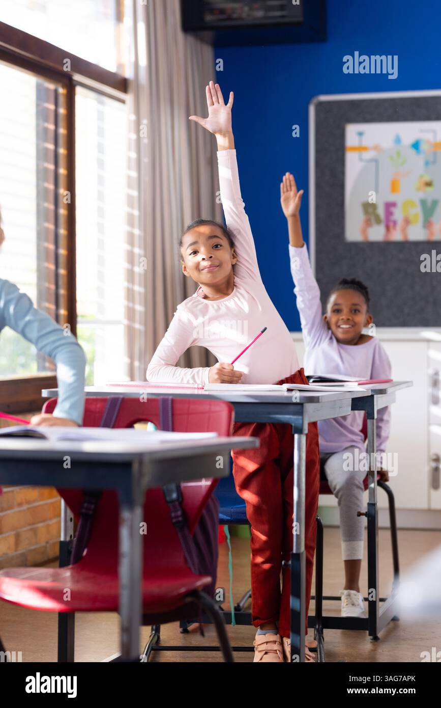 In school, diverse students raising hands while sitting at desks in ...