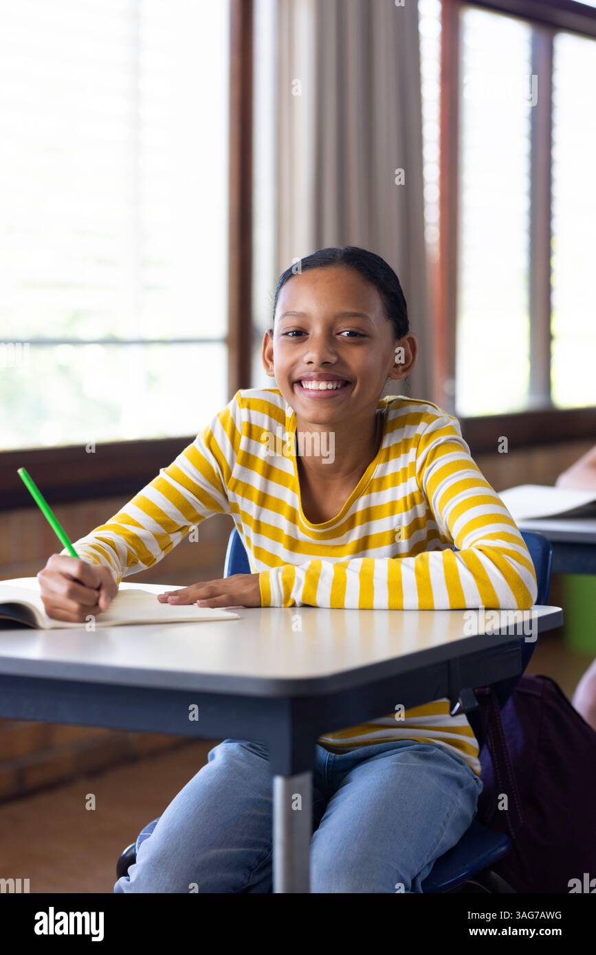In school, girl smiling and writing in notebook at classroom desk Stock ...