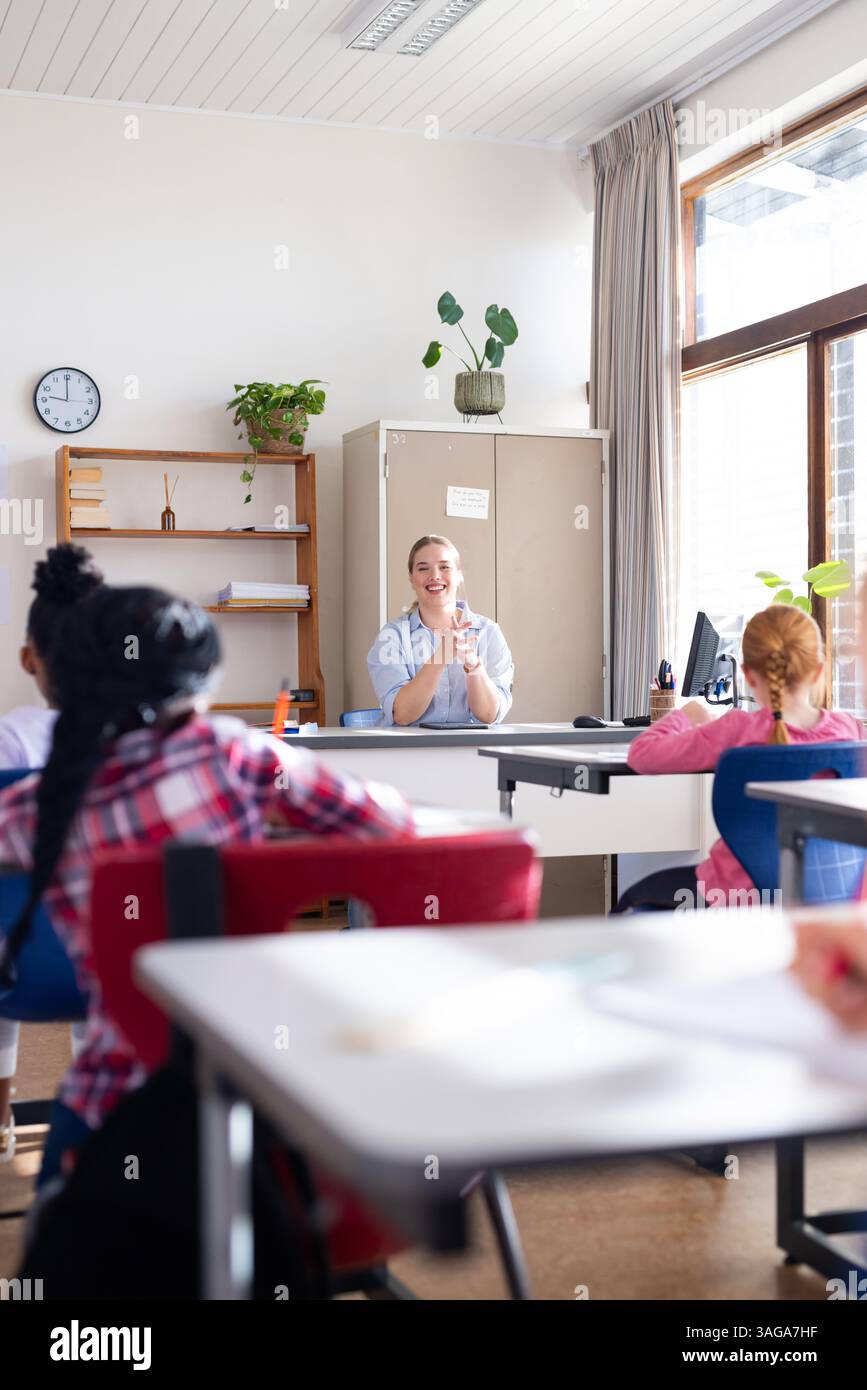 Female teacher clapping hands, engaging diverse students in classroom ...