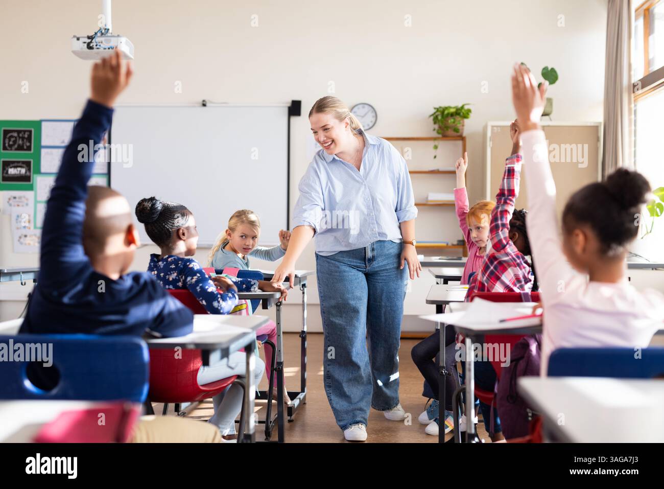 In school, female teacher engaging with diverse students raising hands ...