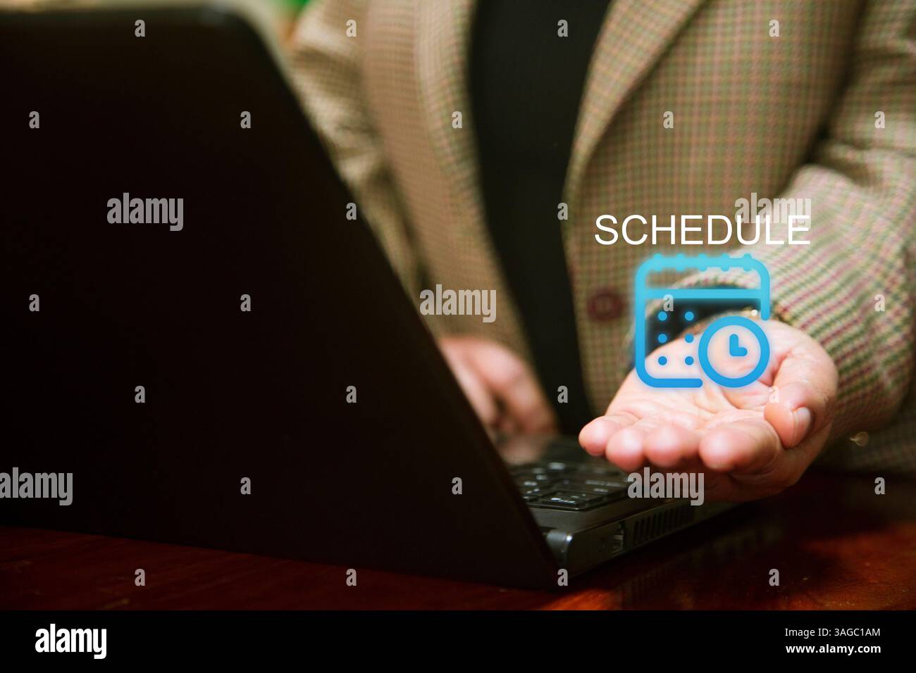 A business person in a checkered blazer works on a laptop, while holding out their hand with a digital calendar and clock icon floating above it, symb Stock Photo