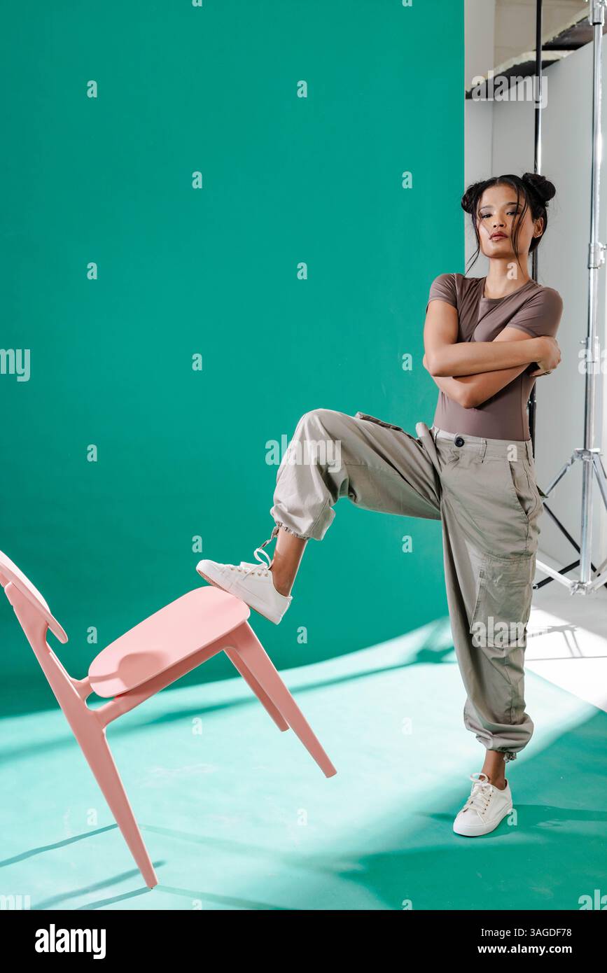 Confident woman in casual outfit balancing chair with foot in studio. Balance, confidence, acrobatics, skill, talent, posing Stock Photo