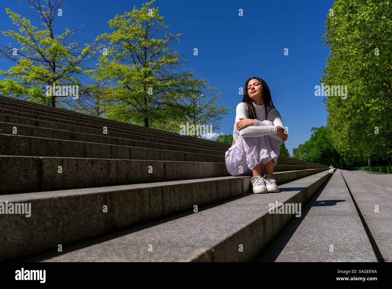 Serene Gen Z woman sitting on concrete stairs and enjoying the spring sunlight Stock Photo