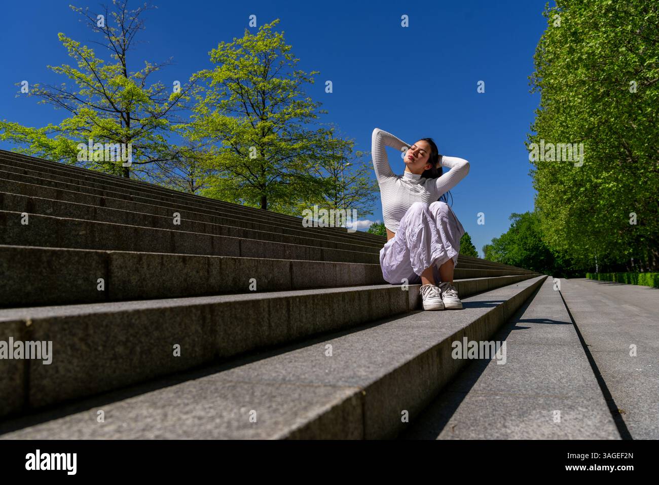Serene Gen Z woman taking a break in the park and enjoying the spring sunlight Stock Photo