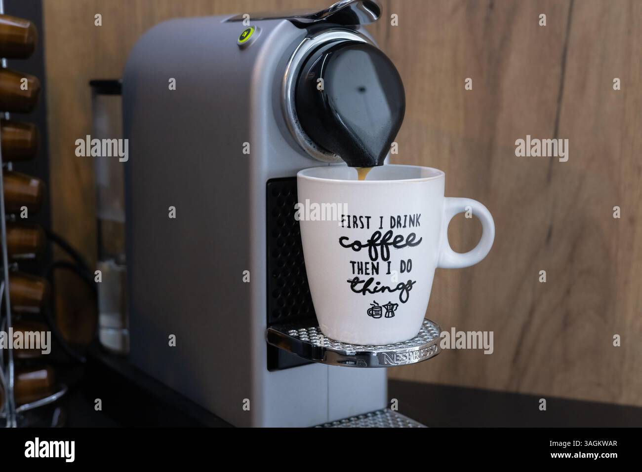 Close-up of a Krups Nespresso coffee machine pouring espresso into a mug with the text first I drink coffee then I do things. Stock Photo