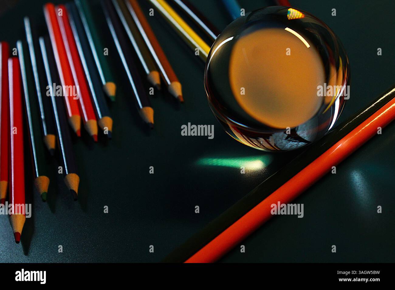 A creative macro shot using a clear glass ball placed among several sharpened colored pencils on a dark surface. Stock Photo