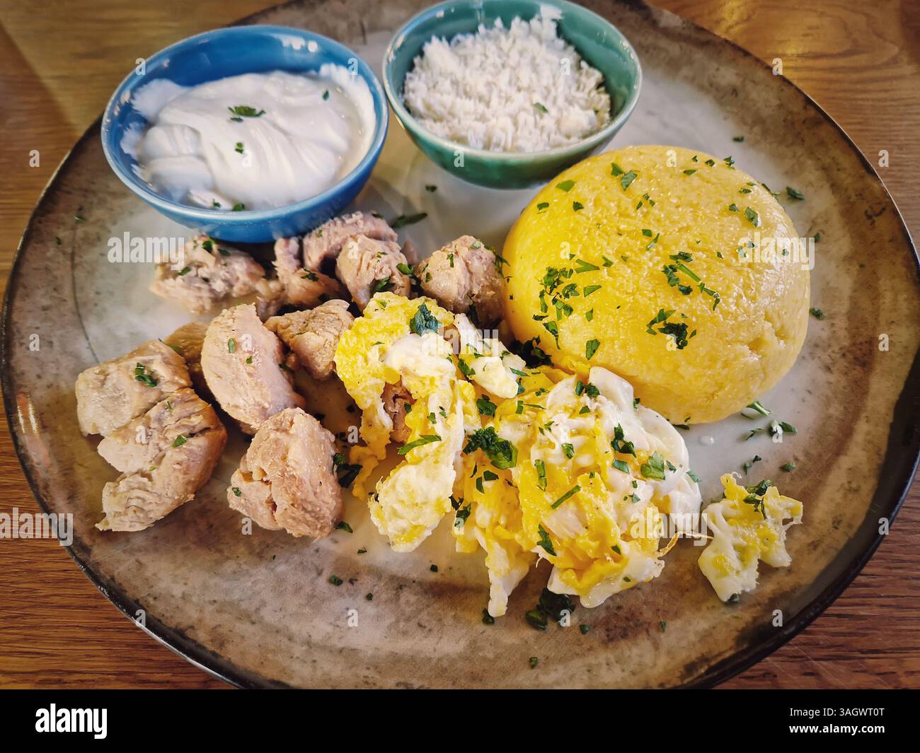 Traditional Moldovan food, meal closeup with pork stew, mamaliga polenta, fried eggs, cheese and sour cream sprinkled with parsley - Smartphone Captured Stock Image
