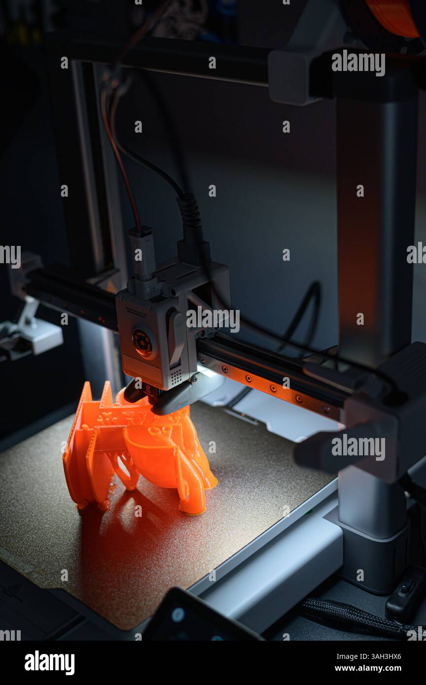 3D Printer Creating Orange Plastic Object on Platform Stock Photo