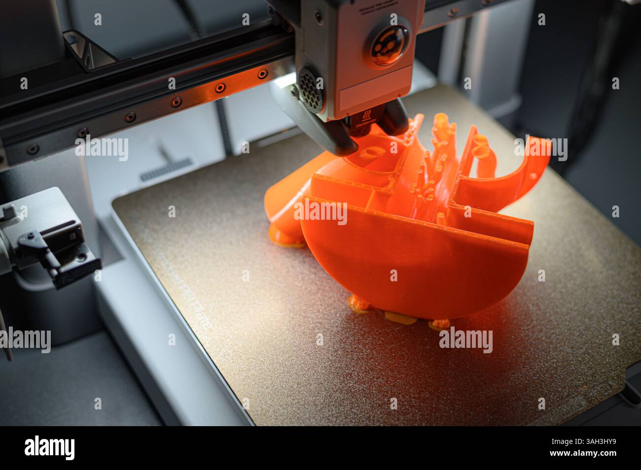 3D Printer Creating Orange Plastic Object on Platform Stock Photo