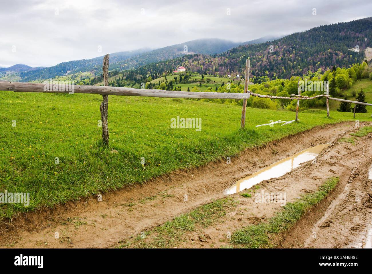 countryside mountain landscape in spring. green nature with cloudy sky. beautiful view with fence along the path through hill in the rain for tourism. Stock Photo