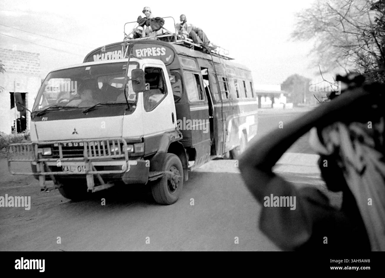 Mar 2, 2015 - Kenya - A matatu and a woman in a dusty road in rural Kenya. Landscape. The infrastructure in Kenya are very poor. The roads are not paved and marked. belongs to the region of Kitui that, in spite of its proximity to the capital, Nairobi, is one of the developed areas less of the country. Nothing else to arrive, after lengths and tedious kilometres of dust and pockets, great posters give the welcome you: Letâ€™s talk, we speak. They are the mirror of a society that moved away of the new technologies, the telephone, and the running water and of the electricity, it has not been abl Stock Photo