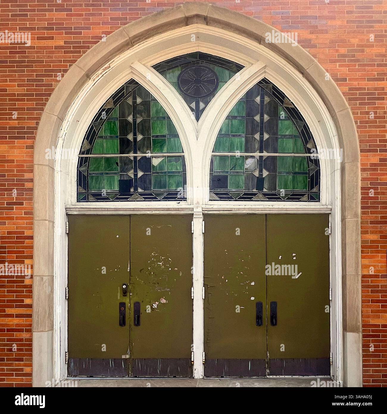 Aged green church doors beneath a large Gothic arch with stained glass windows in geometric patterns, set in a red brick facade in Chicago - Smartphone Captured Stock Image